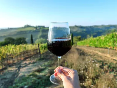 Wine glass over beautiful landscape of Tuscany, with green valley of grapes and hills around. Wine beverage tasting in Italy during harvest.