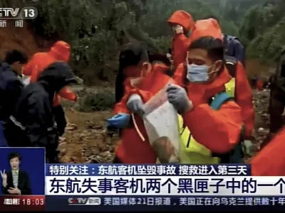 In this image taken from video footage run by China's CCTV, an emergency worker puts an orange-colored "black box" recorder into a plastic bag at the China Eastern flight crash site Wednesday, March 23, 2022, in Tengxian County in southern China's Guangxi Zhuang Autonomous Region. A Chinese aviation official said Wednesday that one of the two "black box" recorders had been found in severely damaged condition, two days after a China Eastern flight crashed in southern China with 132 people on board. (CCTV via AP Video)