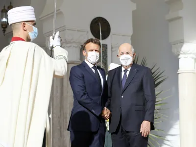 French President Emmanuel Macron, center, shakes hands with Algerian President Abdelmajid Tebboune, Thursday, Aug. 25, 2022 in Algiers. French President Emmanuel Macron is in Algeria for a three-day official visit aimed at addressing two major challenges: boosting future economic relations while seeking to heal wounds inherited from the colonial era, 60 years after the North African country won its independence from France. (AP Photo/Anis Belghoul)