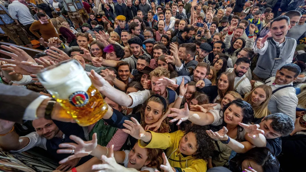 Young people reach out for free beer in one of the beer tents on the opening day of the 187th Oktoberfest beer festival in Munich, Germany, Saturday, Sept. 17, 2022. (AP Photo/Michael Probst)