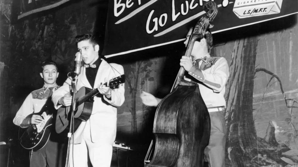 SHREVEPORT, LA - OCTOBER 16: Singer Elvis Presley joins his guitar player Scotty Moore (left) and bass player Bill Black on a weekly broadcast of "Lousiana Hayride" at the Shreveport Auditorium just three months after Elvis left home for the first time on October 16, 1954 in Shreveport, Lousiana. (Photo by Michael Ochs Archives/Getty Images)