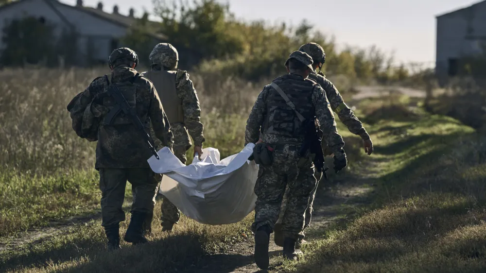 Ukrainian servicemen carry an exhumed body in the recently retaken village of Shandryholove, the Donetsk region, Ukraine, Sunday, Oct. 16, 2022. (AP Photo/LIBKOS)