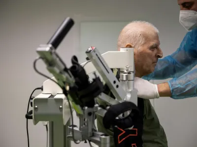 Yannis Ieremias, 70, is assisted to sit on a robotic-assisted hand therapy device at the Theseus Rehabilitation Centre in Athens, Greece, February 1, 2021. Ieremias, who spend more than 50 days in the intensive care unit of an Athens hospital with the coronavirus disease (COVID-19), must undergo therapy to recover from mobility problems caused by his extend hospitalisation. Picture taken February 1, 2021. REUTERS/Alkis Konstantinidis