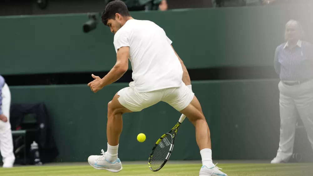 Spain's Carlos Alcaraz plays a shot back between his legs back to Francis Tiafoe of the United States during their third round match at the Wimbledon tennis championships in London, Friday, July 5, 2024. (AP Photo/Alberto Pezzali)