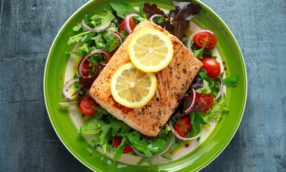 Baked salmon steak with tomato, onion, mix of green leaves salad in a plate. healthy food. / Foto: Drong