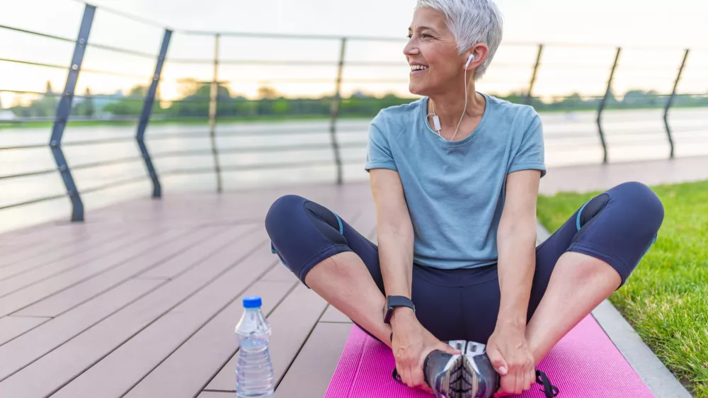 Relaxed athletic mature woman sitting on fitness mat outdoors. Senior Woman Resting After Exercises. Woman on a yoga mat to relax outdoor. Senior lady prefers healthy lifestyle