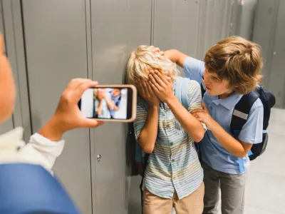 Schoolchildren cruel boys filming on the phone torturing bullying their classmate in school hall. Puberty difficult age