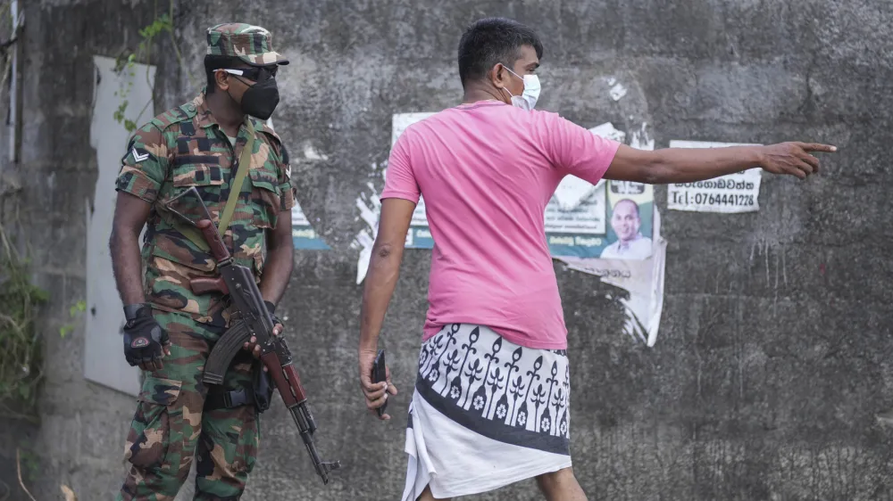 A Sri Lankan man interacts with an army soldier standing guard in a street during a curfew in Colombo, Sri Lanka, Sunday, April 3, 2022. Opposition lawmakers were marching Sunday protesting against the president's move to impose a curfew and state of emergency amid a worsening economic crisis. (AP Photo/Eranga Jayawardena)