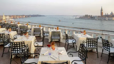 The rooftop terrace of Restaurant Terrazza Danieli at sunset. Small, square, candlelit tables dressed in tablecloths epitomise fine dining in Venice. Spectacular views overlook the Venetian lagoon with tradtional gondolas. 