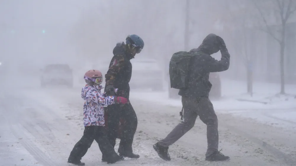 The Firestone family makes their way across Elmwood Avenue in Buffalo, N.Y. after stocking up on supplies at the grocery store, Friday, Dec. 23, 2022. Winter weather is blanketing the U.S. as a massive storm sent temperatures crashing and created whiteout conditions.(Derek Gee /The Buffalo News via AP)