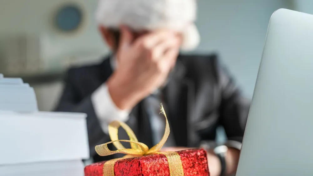 Sad and unhappy businessman with Santa Claus hat crying in office during Christmas holiday season, wrapped present on the desk with selective focus