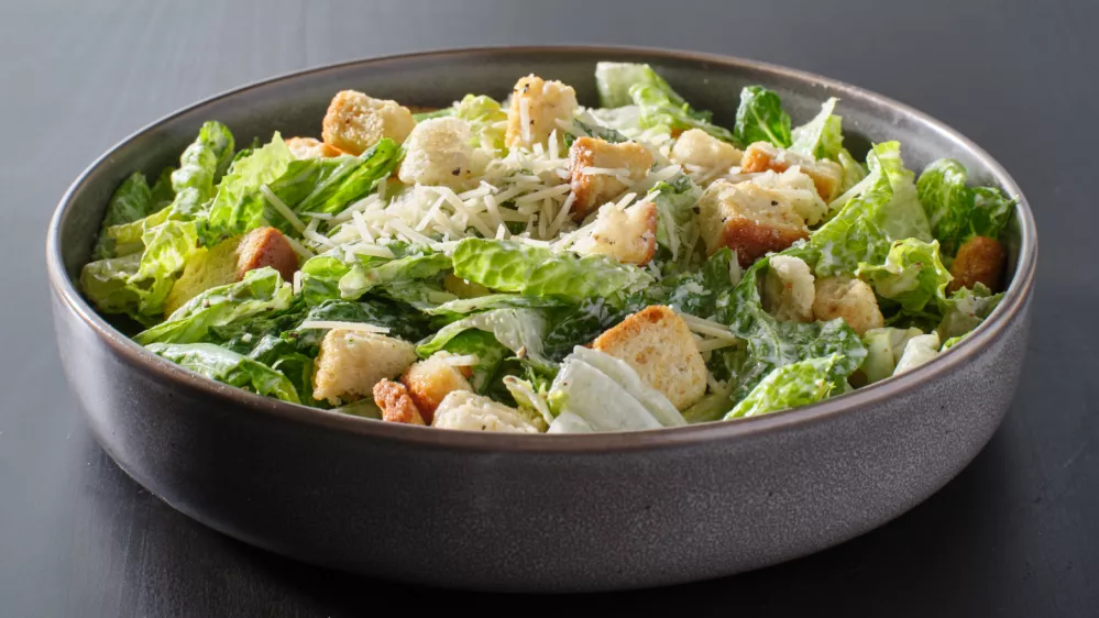 fresh caesar salad with croutons and parmesan cheese in bowl on dark table top / Foto: Rez-art