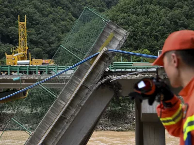 In this photo released by Xinhua News Agency, a rescuer looks at the collapsed bridge as they conduct a search and rescue on a river in Zhashui County in Shangluo City, northwest China's Shaanxi Province, Saturday, July 20, 2024. Chinese authorities say several people have died and more than dozen are missing in the partial collapse of a highway bridge in the northwest of the country following heavy storms and flooding. A similar number are missing in the southwest after dozens of houses were destroyed by storms. (Zou Jingyi/Xinhua via AP)