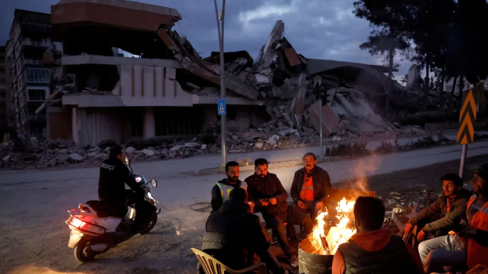 People warm themselves by a fire beside a collapsed building and rubble, in the aftermath of a deadly earthquake, in Antakya, Hatay province, Turkey, February 21, 2023. REUTERS/Clodagh Kilcoyne