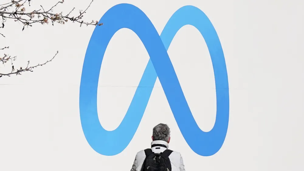 A person stands in front of a Meta sign outside of the company's headquarters in Menlo Park, Calif., Tuesday, March 7, 2023. Facebook's parent Meta will slash another 10,000 jobs and will not fill 5,000 open positions as the social media pioneer cuts costs. (AP Photo/Jeff Chiu)