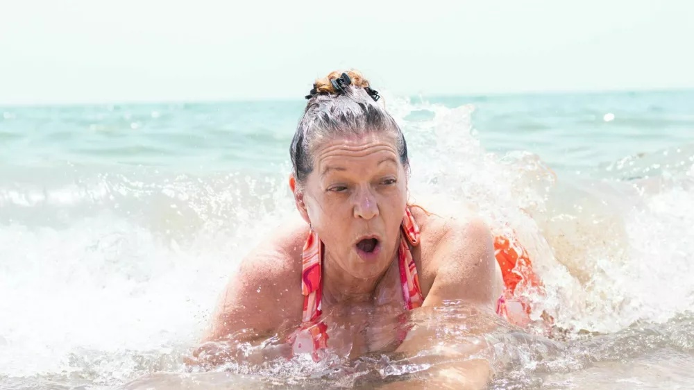 senior adult woman having fun with the waves of the sea on the shore of a beach on summer vacation during a heat wave / Foto: David Petrus Ibars