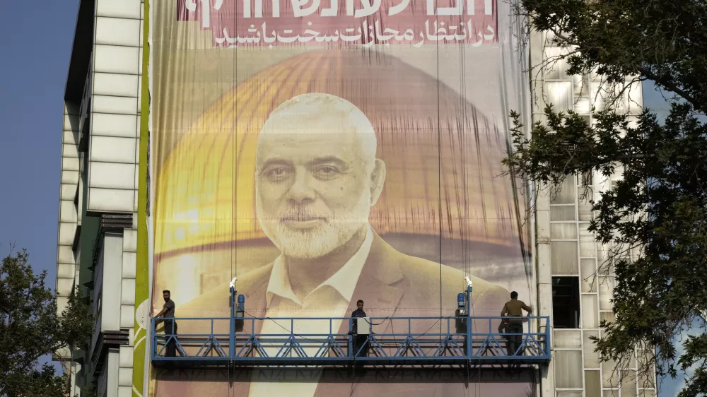 Iranian workers install a huge banner on a wall showing a portrait of Hamas leader Ismail Haniyeh and the Dome of Rock Mosque at the Al-Aqsa Mosque compound of Jerusalem with a sign which reads in Farsi and Hebrew: "Wait for severe punishment," at Felestin (Palestine) Sq. in Tehran, Iran, Wednesday, July 31, 2024. Haniyeh was assassinated in Tehran, Iran's paramilitary Revolutionary Guard said early Wednesday. (AP Photo/Vahid Salemi)