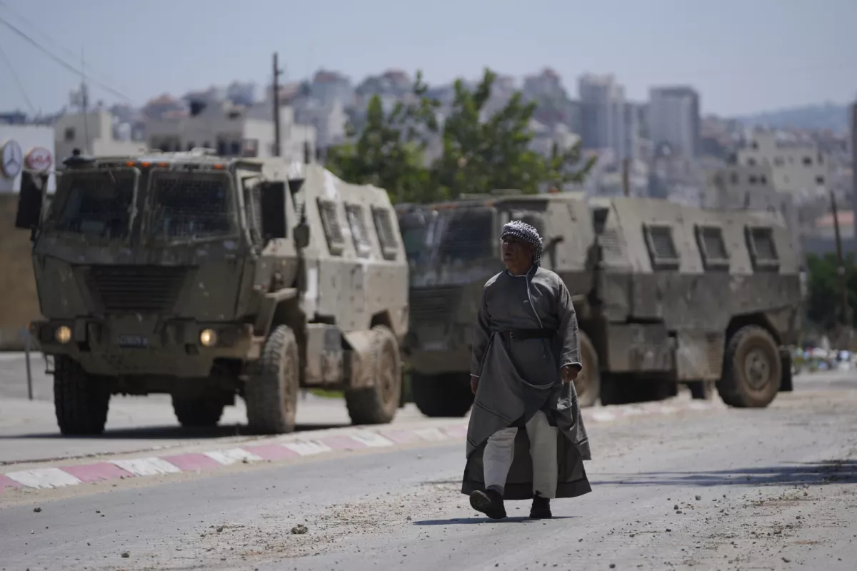 A Palestinian man walks past two army personal carriers during an Israeli army raid in the occupied West Bank refugee camp of Tulkarem, in Tulkarem, Tuesday, July 23, 2024. (AP Photo/Nasser Nasser)