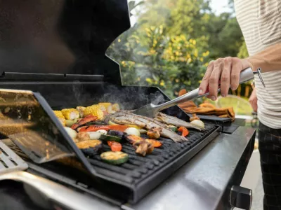 People grilling fish and corn on a modern grill outdoors at sunet, close-up. Cooking food on the open air / Foto: Rosshelen