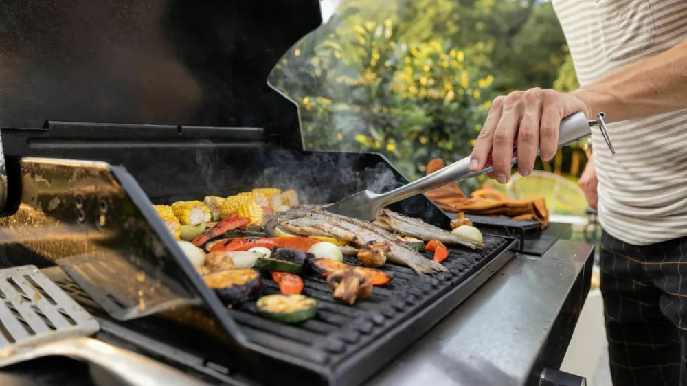 People grilling fish and corn on a modern grill outdoors at sunet, close-up. Cooking food on the open air / Foto: Rosshelen