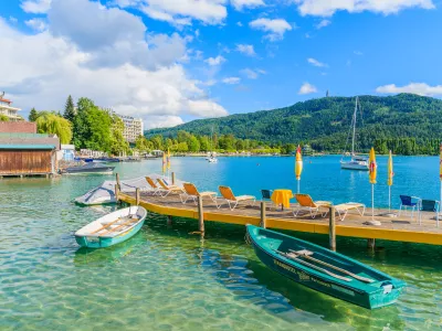 WORTHERSEE LAKE, AUSTRIA - JUN 20, 2015: tourist boats and sunchairs with umbrellas on wooden pier of beautiful alpine lake Wort