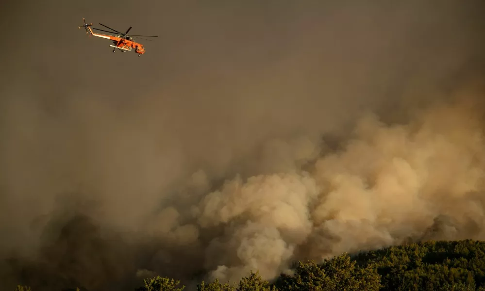 A firefighting helicopter flies over smoke rising from a wildfire burning in the village of Varnavas, near Athens, Greece, August 11, 2024. REUTERS/Hilary Swift