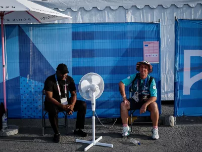 Paris 2024 Olympics - Archery - Women's Individual 1/32 Elimination Rnd - Invalides, Paris, France - July 30, 2024. A security guard and a volunteer cool down near a fan on a hot day. REUTERS/Tingshu Wang   "OLYMPIC BEHIND THE SCENES" FOR THIS STORY. SEARCH "OLYMPIC SIDELINES" FOR ALL STORIES.