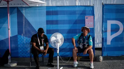 Paris 2024 Olympics - Archery - Women's Individual 1/32 Elimination Rnd - Invalides, Paris, France - July 30, 2024. A security guard and a volunteer cool down near a fan on a hot day. REUTERS/Tingshu Wang   "OLYMPIC BEHIND THE SCENES" FOR THIS STORY. SEARCH "OLYMPIC SIDELINES" FOR ALL STORIES.