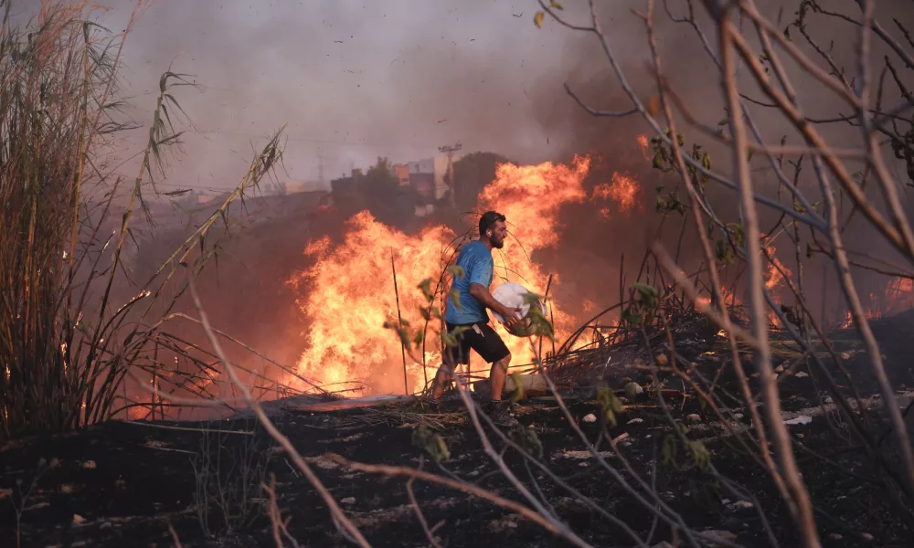 A volunteer tries to extinguish the fire in northern Athens, Monday, Aug. 12, 2024, as hundreds of firefighters tackle a major wildfire raging out of control on fringes of Greek capital. (AP Photo/Aggelos Barai)