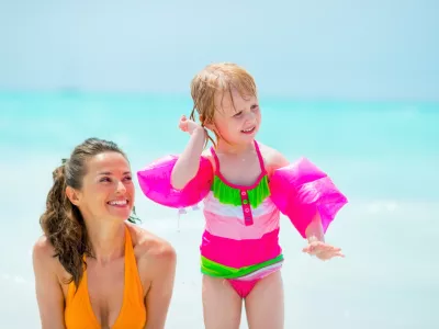 Baby girl shaking out water from ear on beach near mother / Foto: Centralitalliance