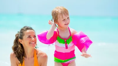 Baby girl shaking out water from ear on beach near mother / Foto: Centralitalliance