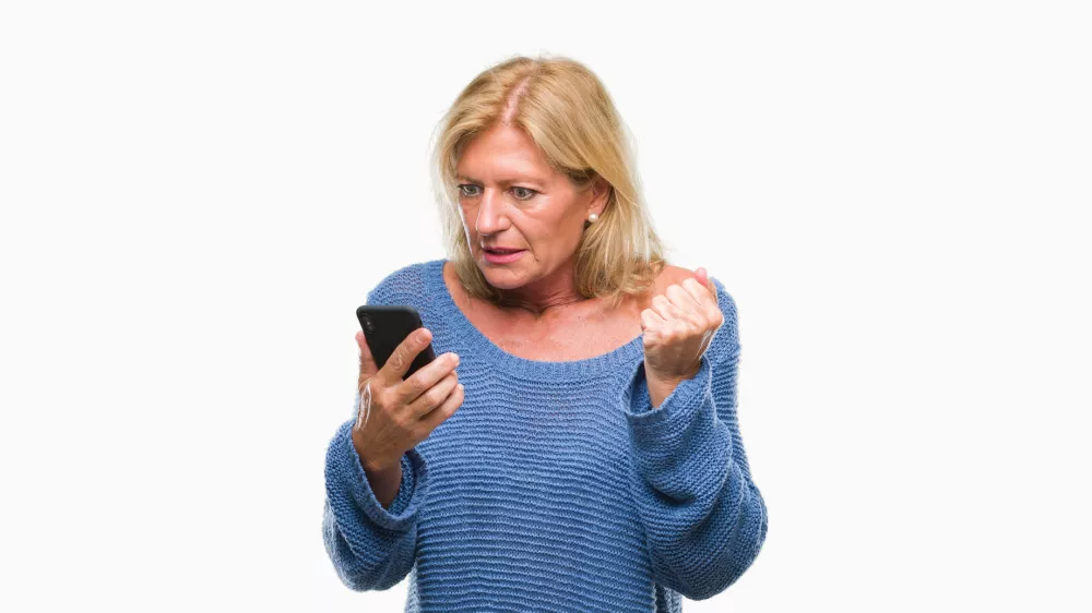 Middle age blonde woman sending message using smartphone over isolated background annoyed and frustrated shouting with anger, crazy and yelling with raised hand, anger concept / Foto: Aaronamat