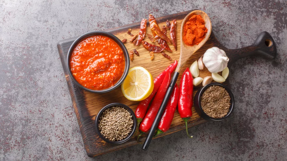 Hot chilli pepper sauce paste harissa, Arabic cuisine adjika on the bowl on wooden board with ingredients closeup. Horizontal top view from above / Foto: Alleko