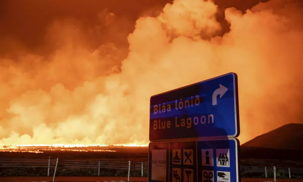 The sign with the direction to the blue lagoon with the new eruption in the background in Grindavik, Iceland, Thursday, Aug. 22, 2024, (AP Photo/Marco di Marco)