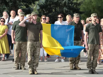 23 August 2024, Ukraine, Kiev: Soldiers stand to attention with the national flag outside the Densianskyi District State Administration on State Flag Day. Photo: -/Ukrinform/dpa