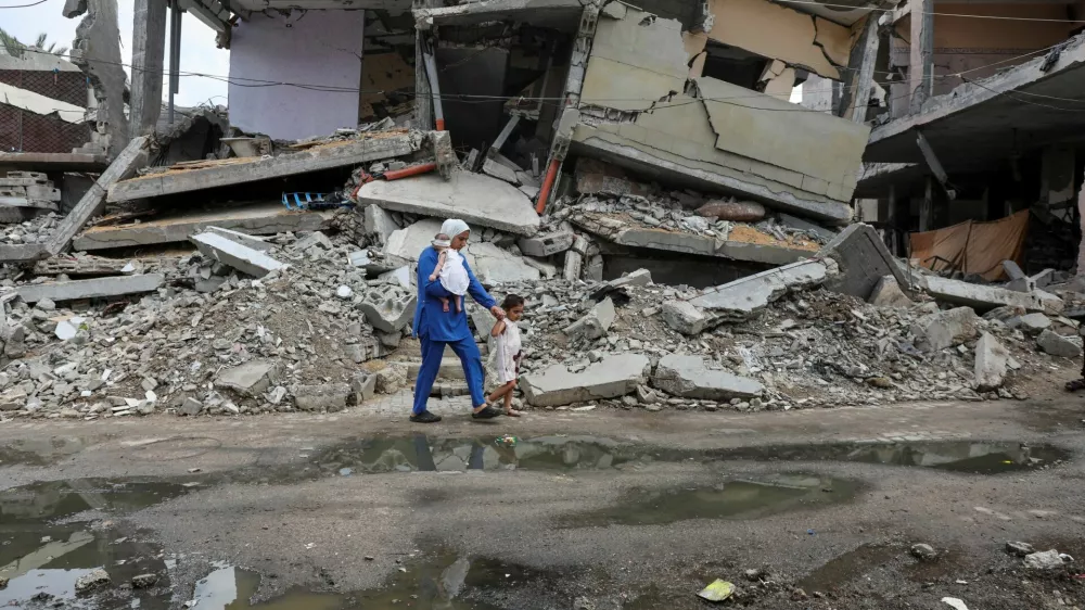 A displaced Palestinian mother, Wafaa Abdelhadi, walks past the rubble of a house destroyed in an Israeli strike as she returns to her shelter with her daughters Lynn and Roueida, after they got vaccinated against polio, in Deir Al-Balah, in the central Gaza Strip September 1, 2024. REUTERS/Ramadan Abed