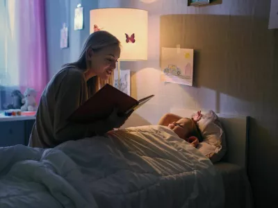 Young Loving Mother Reads Bedtime Stories to Her Little Beautiful Daughter who Goes to Sleep in Her Bed. / Foto: Gorodenkoff