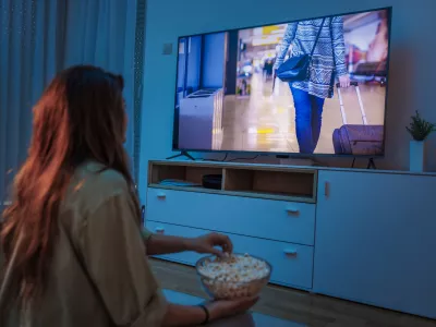 Young woman enjoying leisure time at home at night, watching a movie on TV and eating popcorn / Foto: Getty Images, Vladans