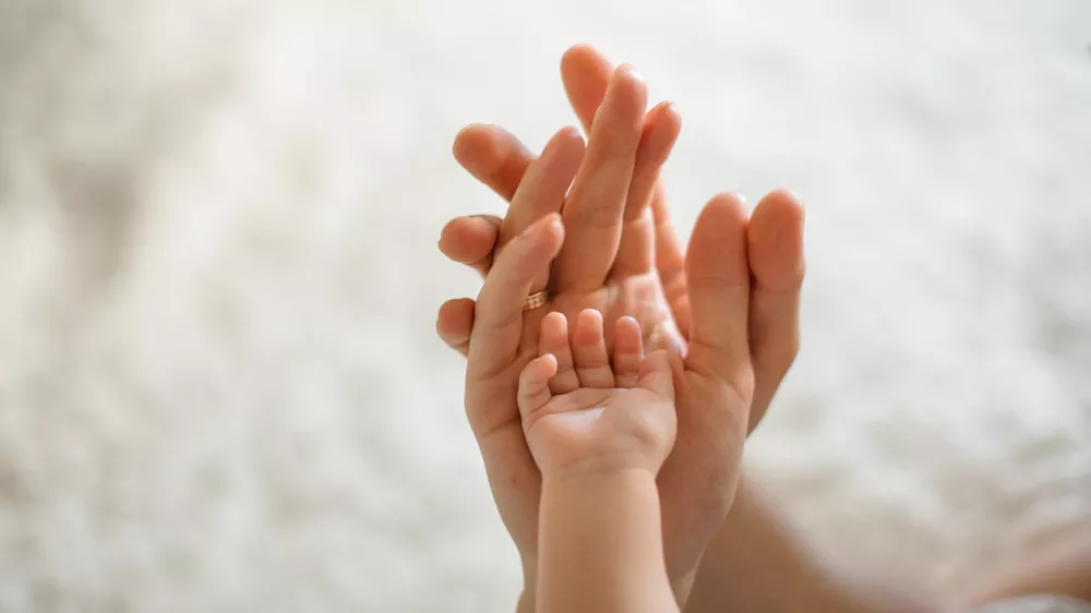 Close up of mother, father and baby join hands on the light background of room