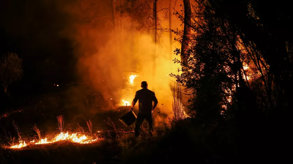 A man holds a bucket during a wildfire in Nelas, Portugal, September 16, 2024. REUTERS/Pedro Nunes