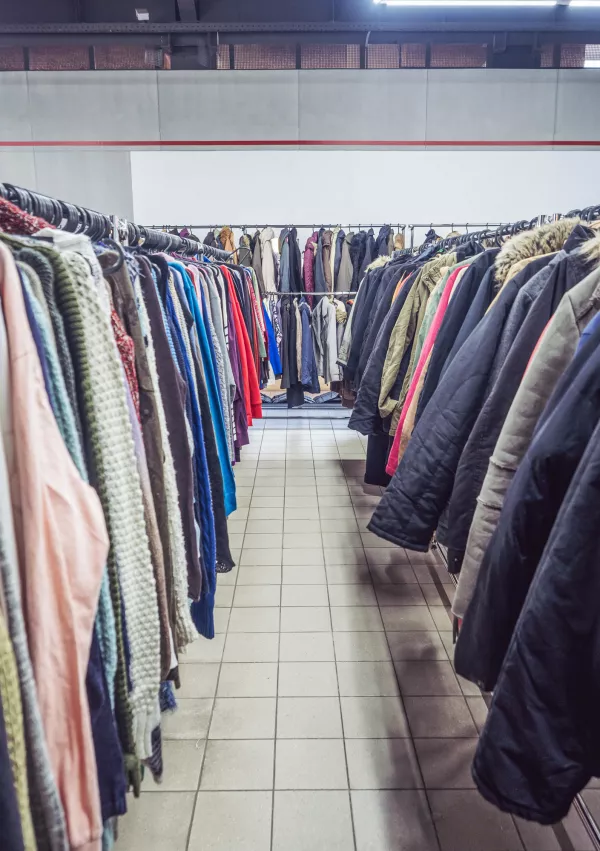 Used clothes on clothing racks at a thrift shop.