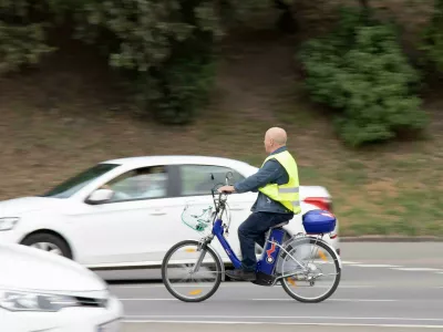 2FP3753 Belgrade, Serbia - May 14, 2021: One senior man wearing fluorescent vest riding an electric bike in city street traffic by the park