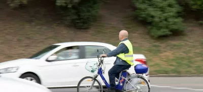 2FP3753 Belgrade, Serbia - May 14, 2021: One senior man wearing fluorescent vest riding an electric bike in city street traffic by the park