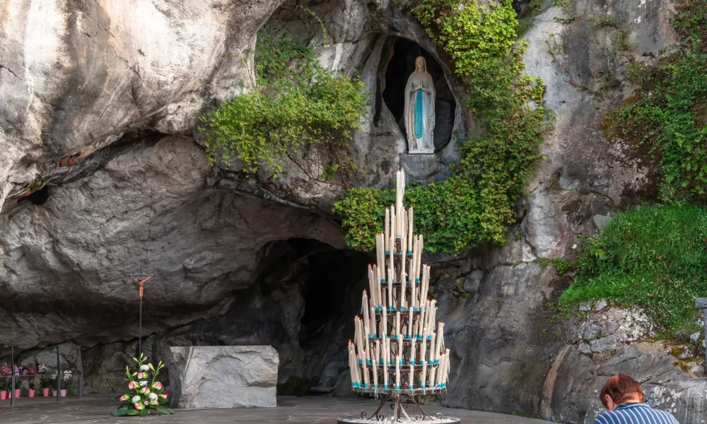 Lourdes, France - August 28, 2021: Woman praying in front of the cave of apparitions of holy Mary in Lourdes