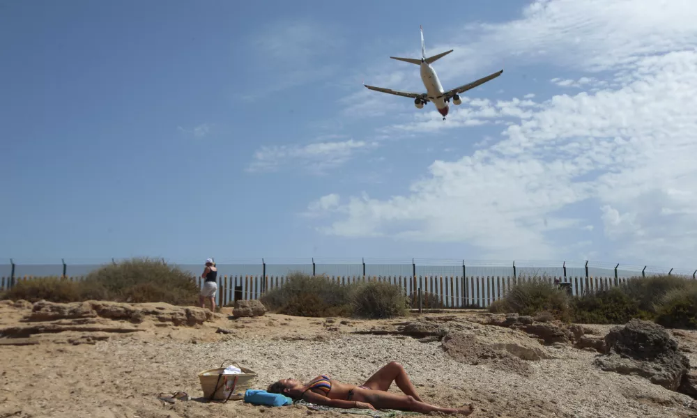 ﻿A woman sunbathes on the beach as an airplane lands at the Balearic Islands capital of Palma de Mallorca, Spain, Wednesday, July 29, 2020. Concerns over a new wave of coronavirus infections brought on by returning vacationers are wreaking havoc across Spain's tourism industry, particularly in the Balearic Islands following Britain's effective ban on travel to the country. (AP Photo/Joan Mateu