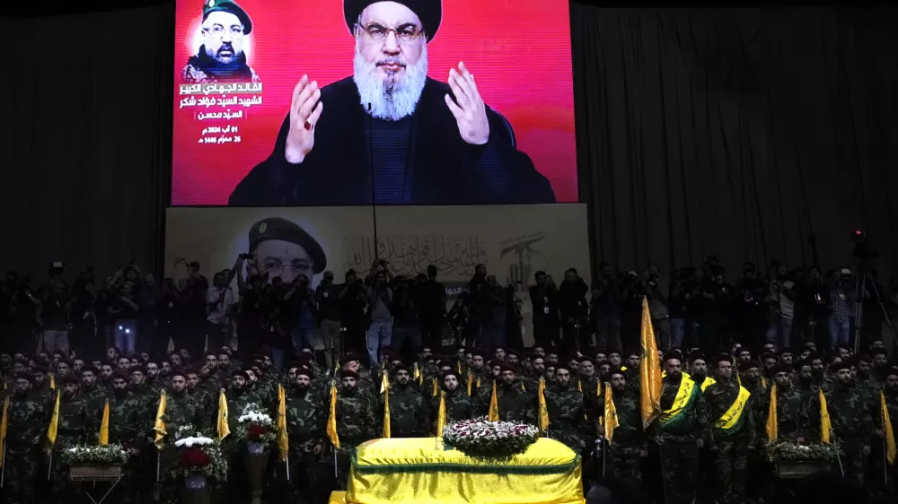 FILE - Hezbollah fighters stand behind the coffin of their top commander Fouad Shukur, who was killed by an Israeli airstrike on July 30, as Hezbollah leader Sayyed Hassan Nasrallah speaks through a screen during Shukur's funeral in a southern suburb of Beirut, Lebanon, Aug. 1, 2024. (AP Photo/Hussein Malla, File)