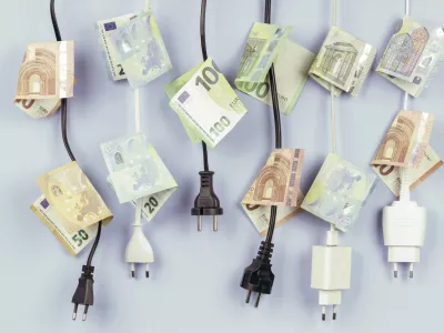 Electric power plugs with Euro banknotes on them hanging on light blue background. Energy efficiency, power consumption, electricity cost, and expensive energy concept. / Foto: Vejaa