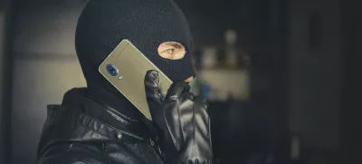 Young adult in black clothes with hidden face. Ill-intended fraudster uses mobile. Fraudster calls. Mobile racket. Hacker hijacks by phone. Cellphone account fraud. Scam / Foto: Diy13