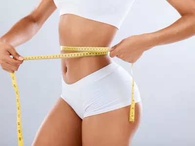 Weightloss, health and woman with measuring tape in a studio for her diet, exercise or wellness. Fitness, body and healthy slim female model checking the measurement of her waist by a gray background / Foto: Jacob Wackerhausen