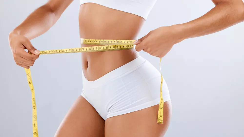 Weightloss, health and woman with measuring tape in a studio for her diet, exercise or wellness. Fitness, body and healthy slim female model checking the measurement of her waist by a gray background / Foto: Jacob Wackerhausen